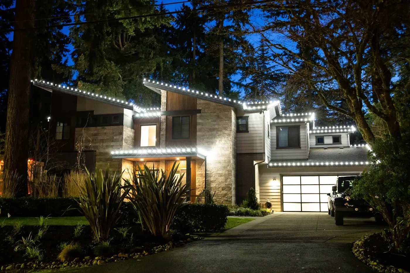 Modern Bellevue home outlined in cool white C9 LED roofline lights among tall evergreens
