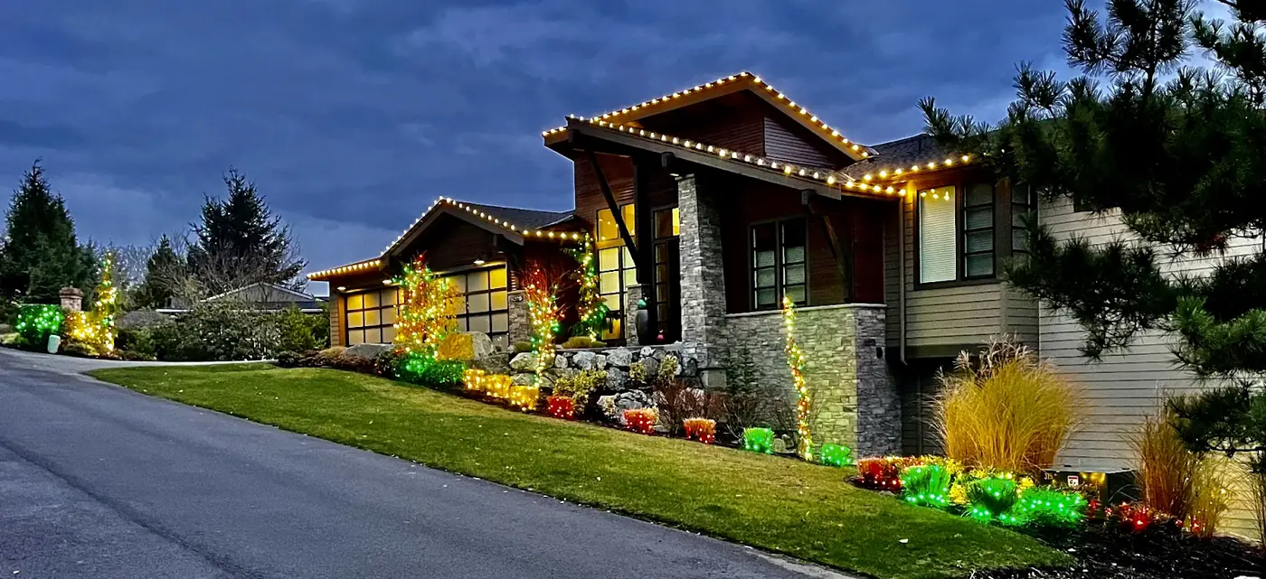 Hillside home with warm white C9 roofline lights and multicolor-lit garden beds